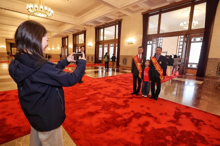 北京人民大会堂，来自辽宁的6岁小朋友李艾桐和家人偶遇受表彰的代表，便邀请代表一起合影。
